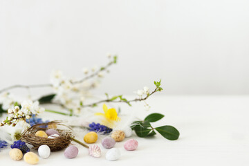 Happy Easter! Stylish easter chocolate eggs in nest, spring flowers, feathers border on white...