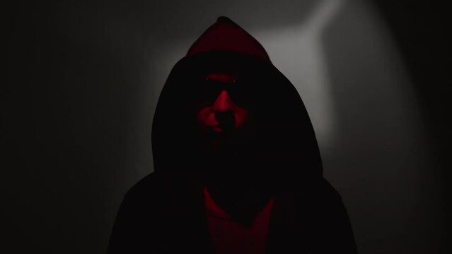 Man in hood and black sunglasses speaking blackmail demands while looking at camera.