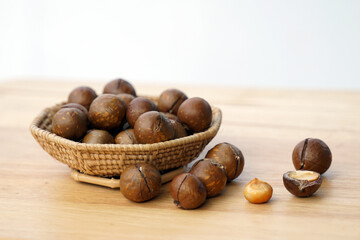 Side view of a basket of roasted macadamia seeds on a wooden table with macadamia nuts spread out. The seeds have flavor. and a fragrant texture Rich in many nutrients.  