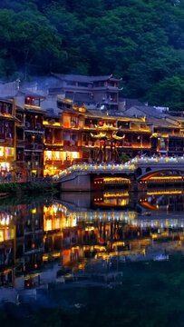 Chinese tourist attraction destination - Feng Huang Ancient Town (Phoenix Ancient Town) on Tuo Jiang River illuminated at night. Hunan Province, China. Camera pan