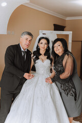 Naklejka premium Happy parents hold the hands of the bride who is getting married and support her, wearing a wedding dress and a long veil.