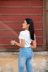 Teenage girl dressed in vintage clothes Including a white t-shirt and pants. Stand facing a wall and pose.