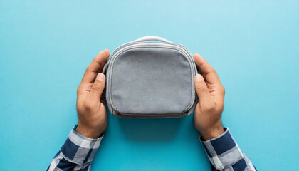 Young adult man hands holding and showing new gray cosmetic travel bag on light blue table background. Pastel color. Closeup. Point of view shot. Top down view - obrazy, fototapety, plakaty