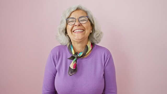 Cheerful grey-haired middle-aged woman playfully making a fish face, standing in a fun, crazy, and comical expression. quirkiness over pink isolated background.