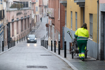 Una operaria municipal de limpieza con su carro y escobas limpia en una calle de una ciudad española.