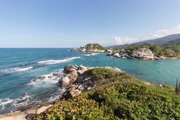 Fototapeta na wymiar Tropical jungle foliage covering rocky mountains with turquoise blue sea and blue sky landscape