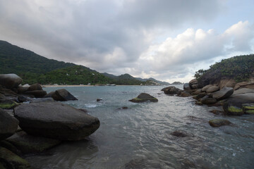 Fototapeta na wymiar Big rocks into caribbean sea with cloudy blue dusk in arrecife beach at tayrona national park