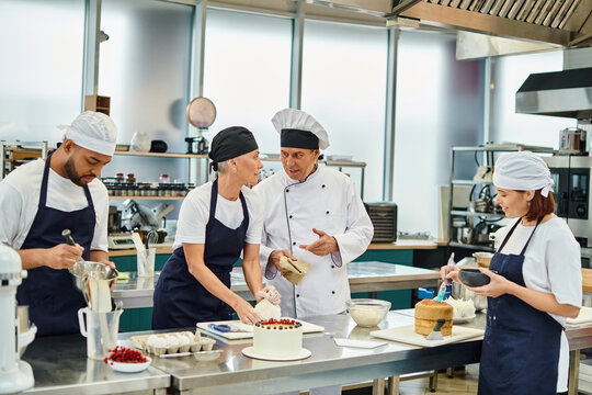mature chief cook in white hat talking to his chef next to her colleagues while on kitchen