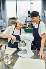 cheerful female chefs in aprons and toques smiling happily and adding oil into mixer, confectionary - obrazy, fototapety, plakaty