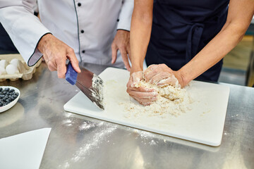 cropped view of mature woman working with dough with chief cook helping her, confectionary