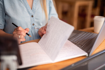 hands of a person working in a coworking space, making notes in a notebook, while working with his laptop computer