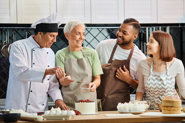 jolly mature chef helping his interracial happy students to decorate delicious cake, cooking courses