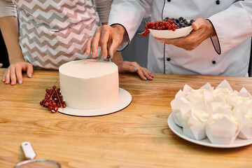 mature chef showing his young student how to decorate tasty cake with berries, cooking courses