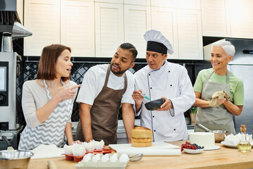 cheerful multiracial people in aprons discussing how to cook with mature chef during lesson
