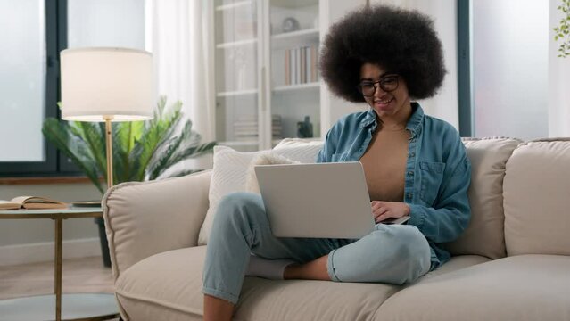 Smiling African American Woman On Couch At Home Using Laptop Smiling Online Work Studying Distance Typing Message Happy Lady Girl Chatting On Computer Browsing Internet Social Media Watch Funny Video