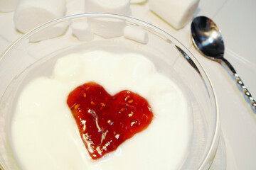 Dessert topped with heart-shaped raspberry jam, stainless steel twisted spoon and Marshmallows on a white plate.