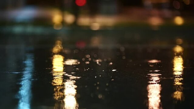 Atmospheric video of rainstorm in a night city. Heavy rain and splashes puddles taken from low point. Large drops break on the pavement in the light of street lamps. Slow motion