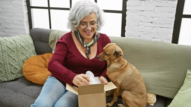 Senior woman unboxing dog comb at home, smiling with pet indoors.