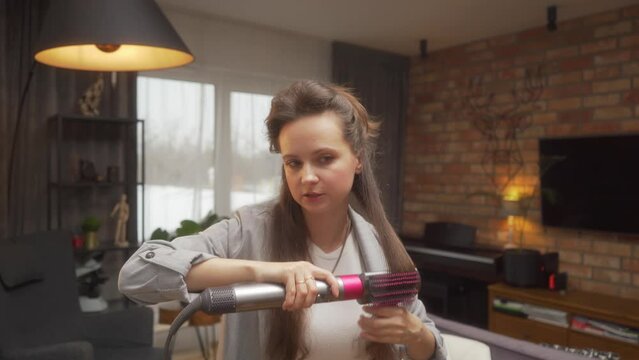 A woman styles her hair with a hairdryer using a nozzle with a soft brush for smoothing. Online hairstyle training for hairdressers and stylists. A tutorial to using hairdryer nozzles at home.