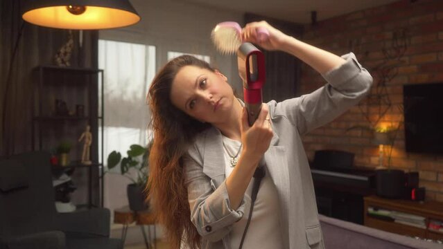 A professional video tutorial on styling long, unruly curly hair with a hairdryer and brush. A woman dries her hair and makes a basal volume with a hairdryer and comb at home.
