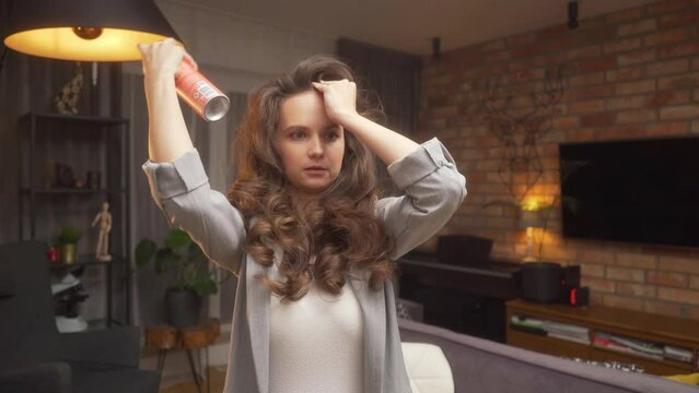 A woman sprinkles bangs and curls with hairspray to create a voluminous styling. In an online webinar, a hairdresser explains how to make voluminous curls on long curly brown hair.