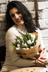 Obraz premium Happy woman drinking coffee and celebrating birthday in coffee shop with bouquet of tulips and bento cake.Birthday concept.Bento cake gift