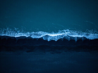 Majestic view of dark blue ocean waves splashing black sand beach, aerial top down shot. Dynamic...