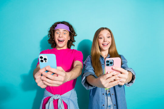 Photo of positive two teenagers takes pictures themselves holding new iphone 15 creating content isolated over aquamarine color background