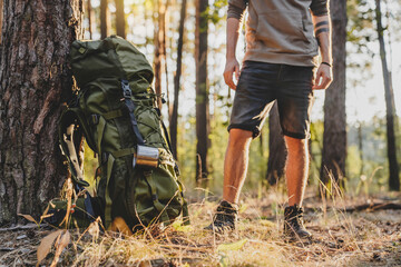 Cropped of male hiker standing near his camping backpack in forest. Away from everything concept....