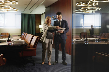 Female lawyer and her young colleague looking through pile of papers standing in conference room
