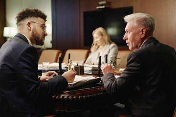 Middle eastern jurist and his senior colleague talking while working with documents in boardroom