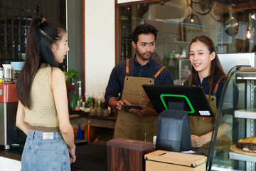 Indian man descent is taking orders from a beautiful Asian customer regularly orders coffee at cafe. and wife working as a barista behind the bar counter in a small coffee shop family business