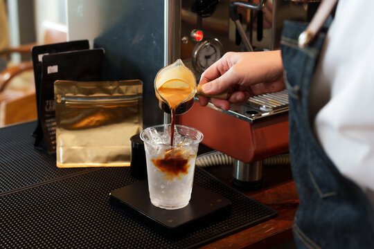 Indian young male baristas He works in small business cafe. He was making glass of drink at the bar counter. He poured the ingredients of drink slowly and prepared it to be served to  customers.