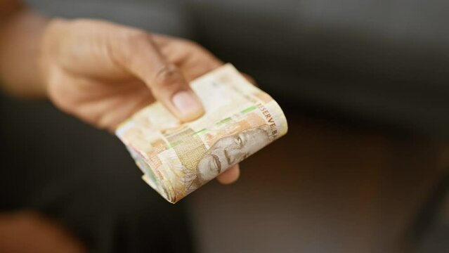 Close-up of a hand presenting south african rand currency indoors, suggesting financial themes and commerce.