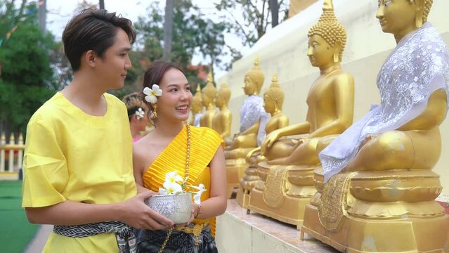 A couple wearing traditional Thai clothing smiles at each other, expressing their joy at the ceremony of bathing a Buddha image during the Thai Songkran festival.