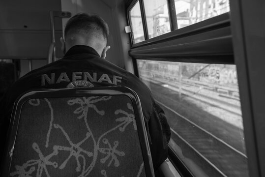 Paris, France - February 21, 2023: Young (unrecognizable; back view) man wearing Naf Naf bomber jacket travels from suburb to city by train line RER A. Naf Naf is popular fashion brand. Black white