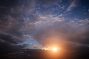 Fototapeta premium Epic Dramatic storm sky with sun. Dark grey black cumulus rain clouds with orange yellow light and sunlight, thunderstorm