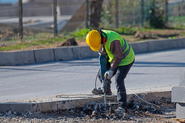A man works with an air hammer on a road construction site.