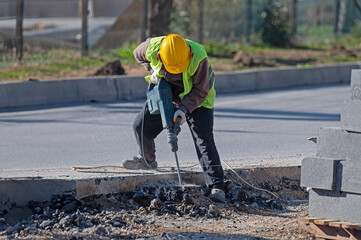 A man works with an air hammer on a road construction site.