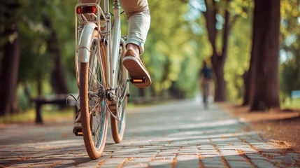 Tuinposter close-up of a person riding a bicycle on a sunlit path through a lush green forest © MP Studio