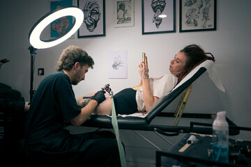 Young Woman Getting a Tattoo on Her Leg From a Professional Artist in a Studio