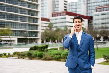 A Hispanic businessman is engaging in a conversation on his mobile phone, smiling subtly with an...