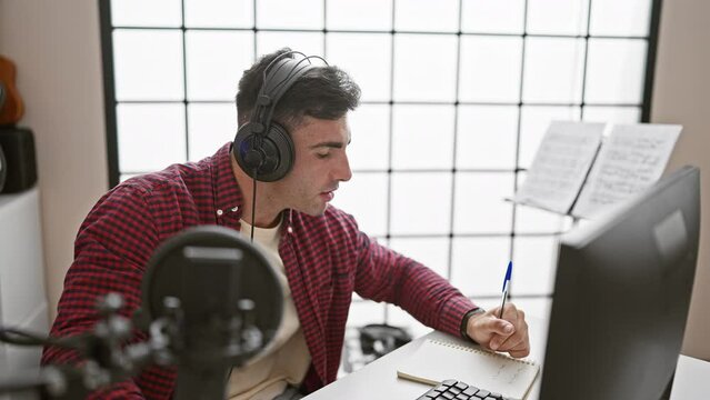 Young, handsome hispanic man, a talented musician, seriously composing a soulful song and singing in an acoustic atmosphere of a music studio, taking notes on music sheets