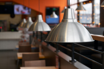 Fragment of restaurant interior with metal hanging lampshades over tables as background image. Copy...