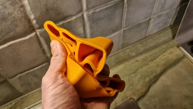 a man crushes a silicone mold in his hand. ice cube in orange color is soft and flexible. strength is not decisive, ice form