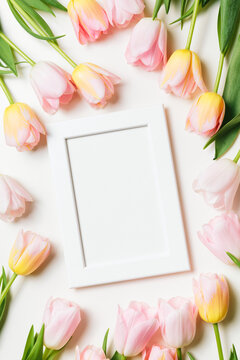 Light pink and yellow blooming tulips flowers row and white picture frame over white background. Spring holiday banner, happy easter card, mothers day concept. Flat lay, top view, copy space