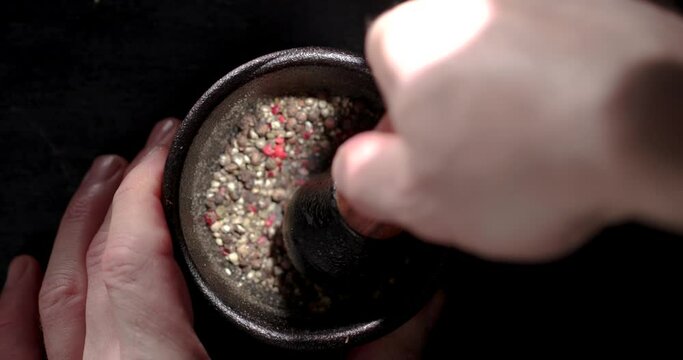 Chef grinding pepper granules in a mortar. Focusing on the mortar.