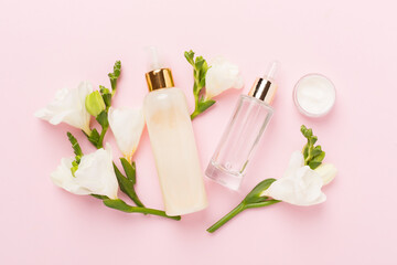 Facial cosmetic products with freesia flowers on color background, top view