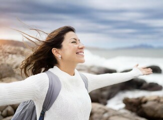 Woman with outstretched arms. Enjoying the wind and breathing fresh air on the rocky beach.
