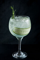 glass of gin and tonic with cucumber and rosemary on black background